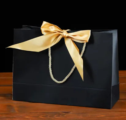 Bowknot Square Paper Bag with a gold satin bow and rope handles on a wooden surface.